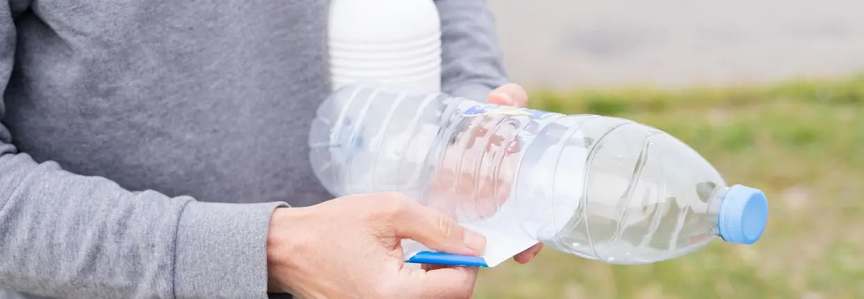 Una mano separa l'etichetta di carta dalla bottiglia di plastica