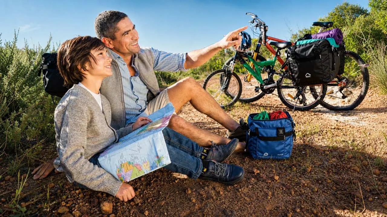 Un adulto e un bambini si riposano con la bici carica di sacche accanto