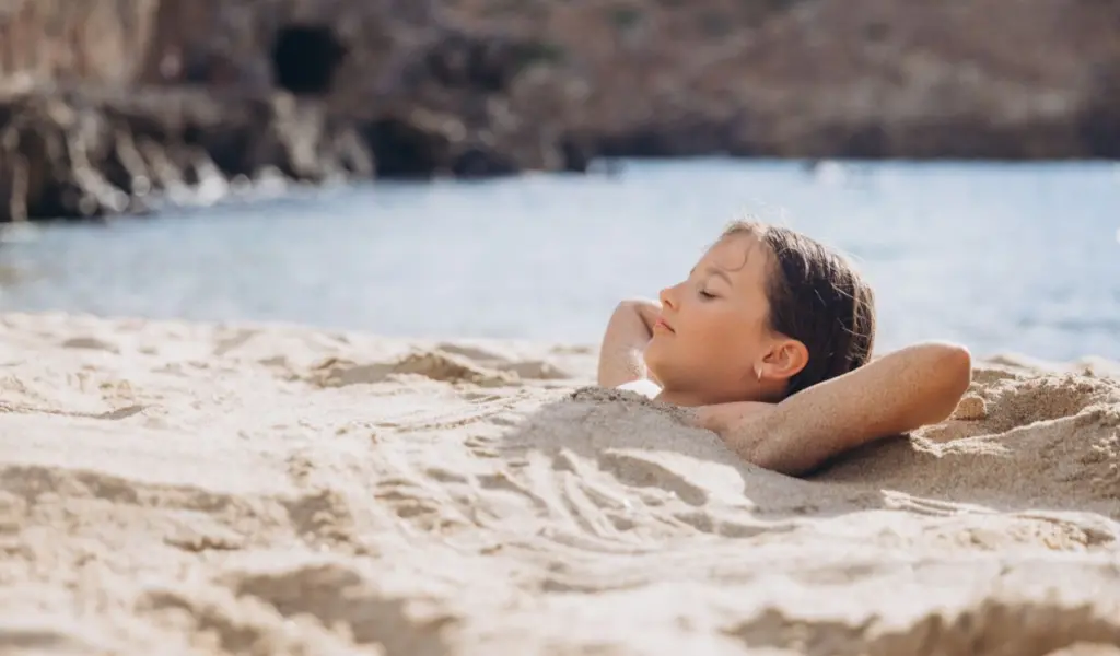 Un bambino in riva al mare con il corpo sotto la sabbia, sotto il sole