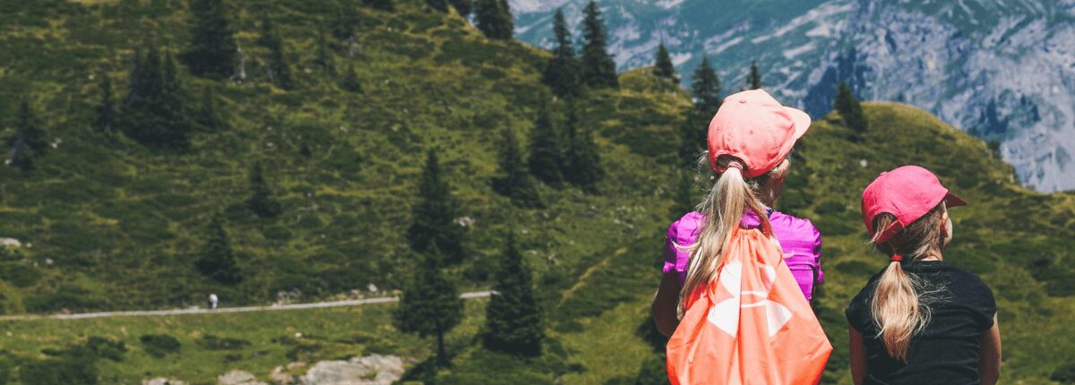 paesaggio di alta montagna con di spalle due bambine escursioniste, estate in sicurezza