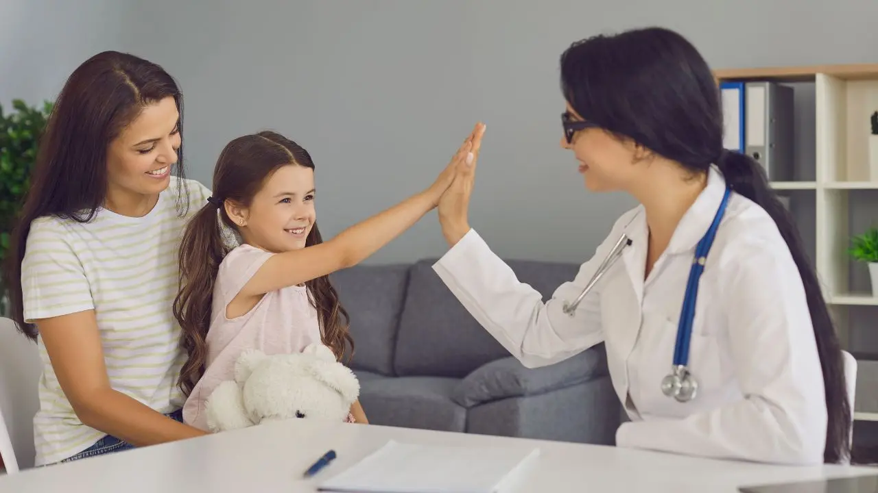 Una bambina dà il cinque alla dottoressa durante una visita di controllo per l'helicobacter, con la madre accanto.